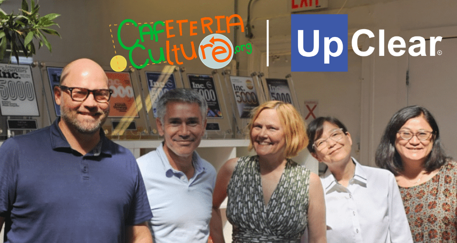 Five people stand smiling indoors beneath Cafeteria Culture and UpClear logos, with framed awards displayed on the wall in the background.